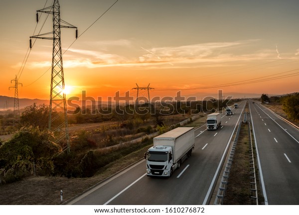 Convoy of\
White transportation  trucks in line as a caravan or convoy on a\
country highway under an amazing sunset\
sky