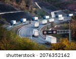 Convoys or caravans of transportation trucks on a curvy highway near tunnel entrance. Highway transit transportation with rows lorry trucksin the Autumn or Fall scenery
