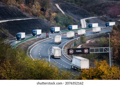 Convoys Or Caravans Of Transportation Trucks On A Curvy Highway Near Tunnel Entrance. Highway Transit Transportation With Rows Lorry Trucksin The Autumn Or Fall Scenery
