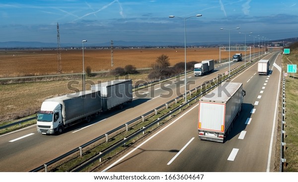 Convoys\
of transportation trucks passing on a highway on a bright blue day.\
Highway transportation \
with white lorry\
trucks
