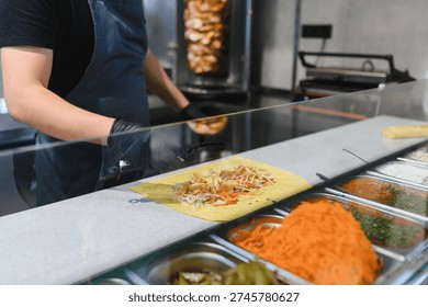 Cook adding chicken and vegetables on a lavash or pita bread, preparing a shawarma or kebab with various ingredients in a street food stall