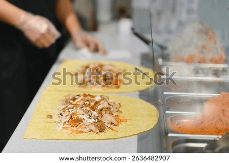 Cook adding chicken and vegetables on a lavash for preparing a shawarma or kebab in a fast food restaurant of oriental cuisine