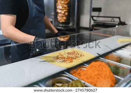 Cook adding chicken and vegetables on a lavash or pita bread, preparing a shawarma or kebab with various ingredients in a street food stall