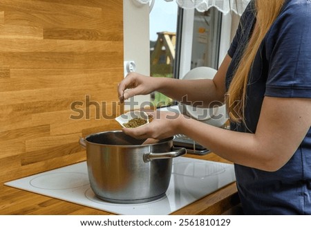 A cook adding spices to a boiling soup in a metal pot.