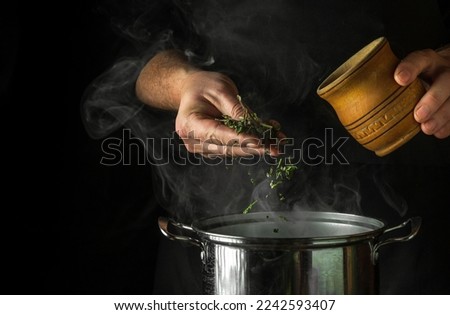 The cook adds dried herbs to boiling water in a pot to make a vitamin drink. Idea from traditional medicine with space for advertising on black background