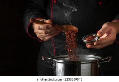 The cook adds dry seasonings to a pot of boiling food. Retsoran kitchen cooking concept with advertising space on black background. - Shutterstock ID 2238569843
