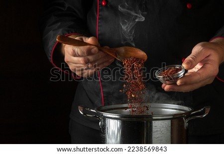 The cook adds dry seasonings to a pot of boiling food. Retsoran kitchen cooking concept with advertising space on black background.