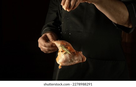 The cook adds salt to a raw chicken leg. The concept of cooking a meat dish for lunch on a black background. - Powered by Shutterstock