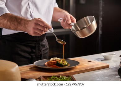 Cook in apron adding some sauce to dish. Cropped chef preparing food, meal, in kitchen, chef cooking, Chef decorating dish, closeup - Shutterstock ID 1927957907