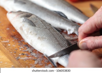 Cook cleaning a sea bass on a wooden cutting board