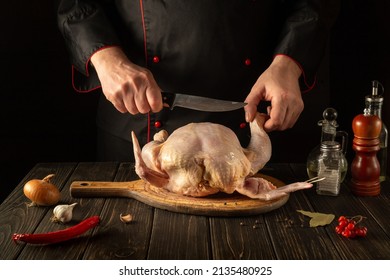 The Cook Cuts Raw Broiler Chicken With A Knife. Cooking A National Dish In The Restaurant Kitchen With Chicken.