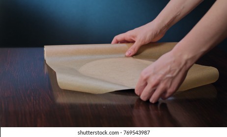 Cook Cutting A Section Of Greaseproof Non-stick Baking Paper With Scissors. Close-up Shot Against A Dark Blue Background