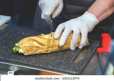 Cook In Disposable Gloves Cuts Sandwich.