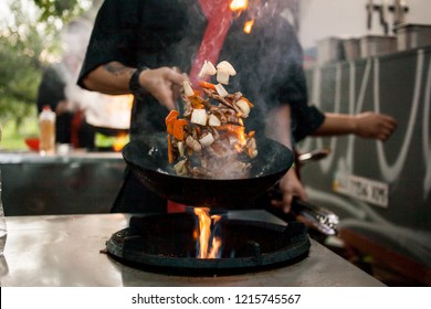 Cook Fries Vegetables In A Wok Pan On Fire. Chef Is Stirring Vegetables In Wok. Chef Cooking With Flame In A Frying Pan. Fire Burns In The Pan. 