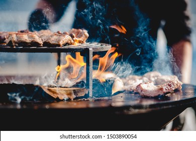 Cook grills steaks and pork ribs open fire. Turns meat over with tongs. Street food concept.