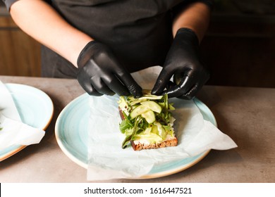 Cook Hands Preparing And Making Sandwich. Preparing Healthy Vegetarian Bruschettas In Dark Gloves. Sandwich With Soft Cheese, Arugula And Cucumber