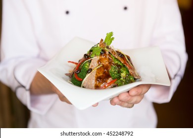 Cook Holding Plate With Food In Welcoming Gesture