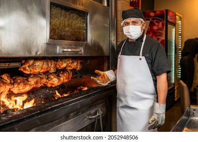 Cook looking at camera next to grill with stack of grilled chicken on a skewer in a restaurant.