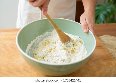 Cook mixing ingredient and wheat flour with wooden spoon in ceramic bowl. Dough preparation for homemade pastry and bread. Studio shot. Side view. Cooking and baking at home concept