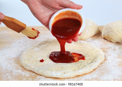 Cook Pouring Tomato Sauce Over Pizza Dough
