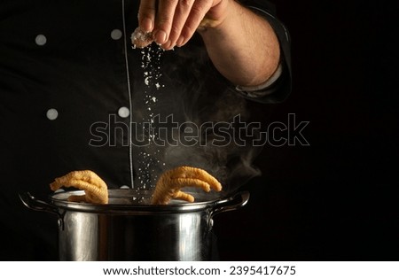The cook pours salt into a pan with boiling chicken legs. The concept of preparing a delicious rich broth in a restaurant kitchen.