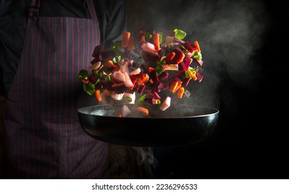 The cook prepares food in a hot pan with steam on a black background. The concept of restaurant and hotel service - Shutterstock ID 2236296533