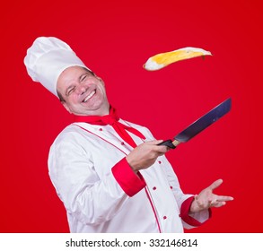 Cook Throw Fried Egg On A Frying Pan. Cheerful Chef Juggles With Omelet On Pan. Master Chef Throws Fried Egg In Pan On Red Background. Friendly Cook Fried Egg. Laughing Cook Fried Egg Flying Over Pan.