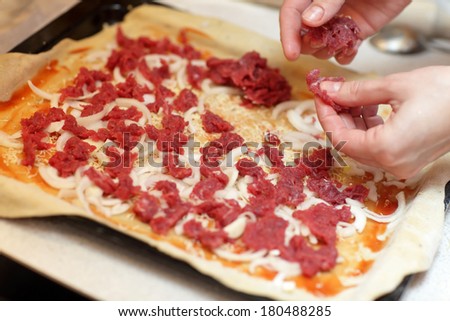 Cook topping pizza with slices of meat