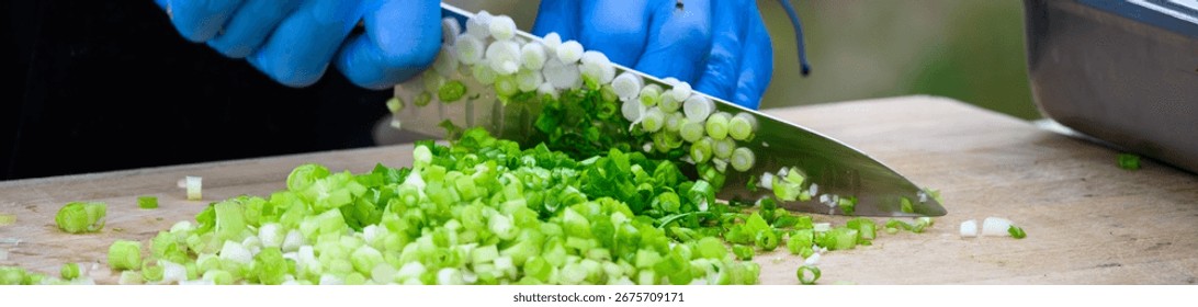 Cook using a chefs knife to slice fresh organic green onions to use as an ingredient, part of luau dinner preparations 
