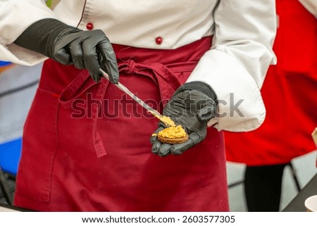 cook in work clothes while preparing snacks. cook in gloves prepares food in a restaurant. snack on shortcrust pastry with egg paste.