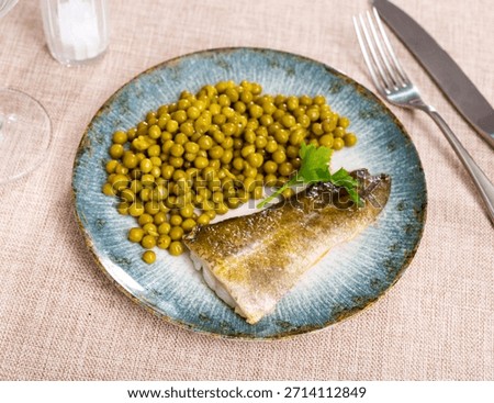 Cooked appetizing cod with a sprig of parsley and green peas on a blue ceramic plate. Bacalao fish for a delicious lunch