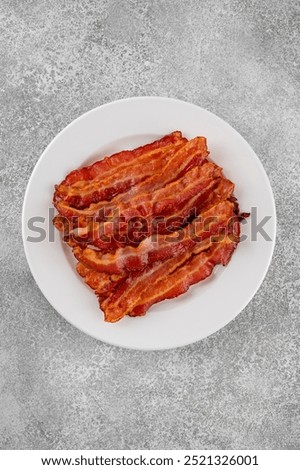 Cooked bacon for breakfast on a white plate on a gray concrete background. Top view, copy space