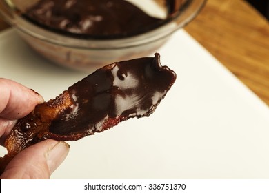 Cooked Bacon Slice Covered In Dark Chocolate Ganache With Glass Chocolate-filled Bowl In The Background