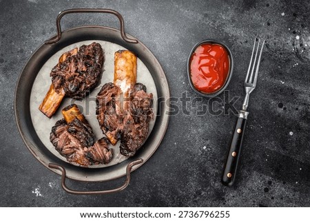 Cooked beef ribs slow cooked until tender with bone and sauce. BBQ style beef plate ribs on dark stone background with copy space