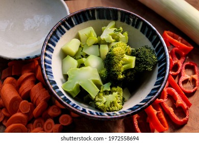 Cooked Broccoli In A Bowl, With Fresh Vegetables Next To It.