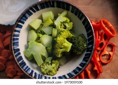 Cooked Broccoli In A Bowl, With Fresh Vegetables Next To It.