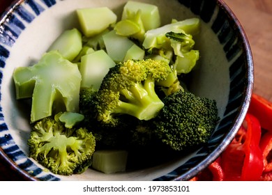 Cooked Broccoli In A Bowl, With Fresh Vegetables Next To It.