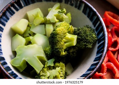 Cooked Broccoli In A Bowl, With Fresh Vegetables Next To It.