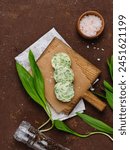 Cooked butter with wild garlic, parsley and salt on a wooden board on a brown concrete background. Snack butter for spreading and steaks. Recipes wild garlic, greens