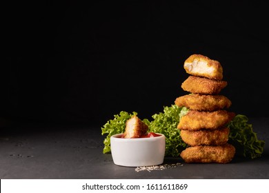 Cooked chicken nuggets in breadcrumbs with lettuce and a bowl of ketchup on a dark background with place for text.
