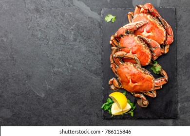 Cooked crabs on black plate served with white wine, black slate background, top view