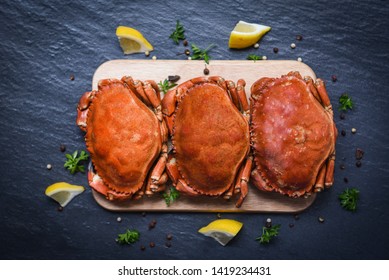 Cooked crabs on wooden board with lemon on plate served on dark plate top view / stone crab steamed seafood 