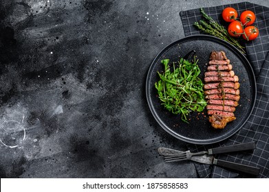 Cooked Grilled Strip Loin Steak, Marbled Beef Meat With Arugula. Black Background. Top View. Copy Space.