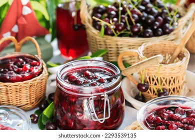 Cooked homemade cherry jam in glass jar on white wooden table outdoors, fresh cherry jam close up, food and healthy eating concept