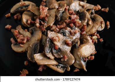 Cooked mushrroms with ham pieces on a black plate
