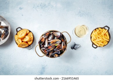 Cooked mussels with French fries and toasted bread, with a glass of white wine, top shot on a slate background with copy space - Shutterstock ID 2166951465