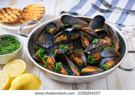Cooked mussels with lemon and parsley on wooden table, selective focus. Ready mussels in a pan on a white wooden table.