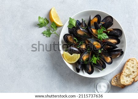 cooked mussels with parsley and lemon in white bowl, top view, copy space