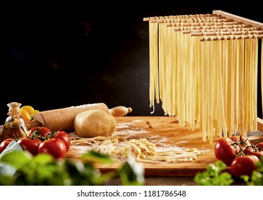 Cooked noodles hanging on wooden rack over cutting board with rolling pin behind foreground vegetables - Powered by Shutterstock