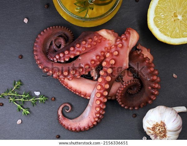 Cooked octopus tentacles on black slate plate served\
with spices, garlic, lemon and olive oil, top view of delicious sea\
food